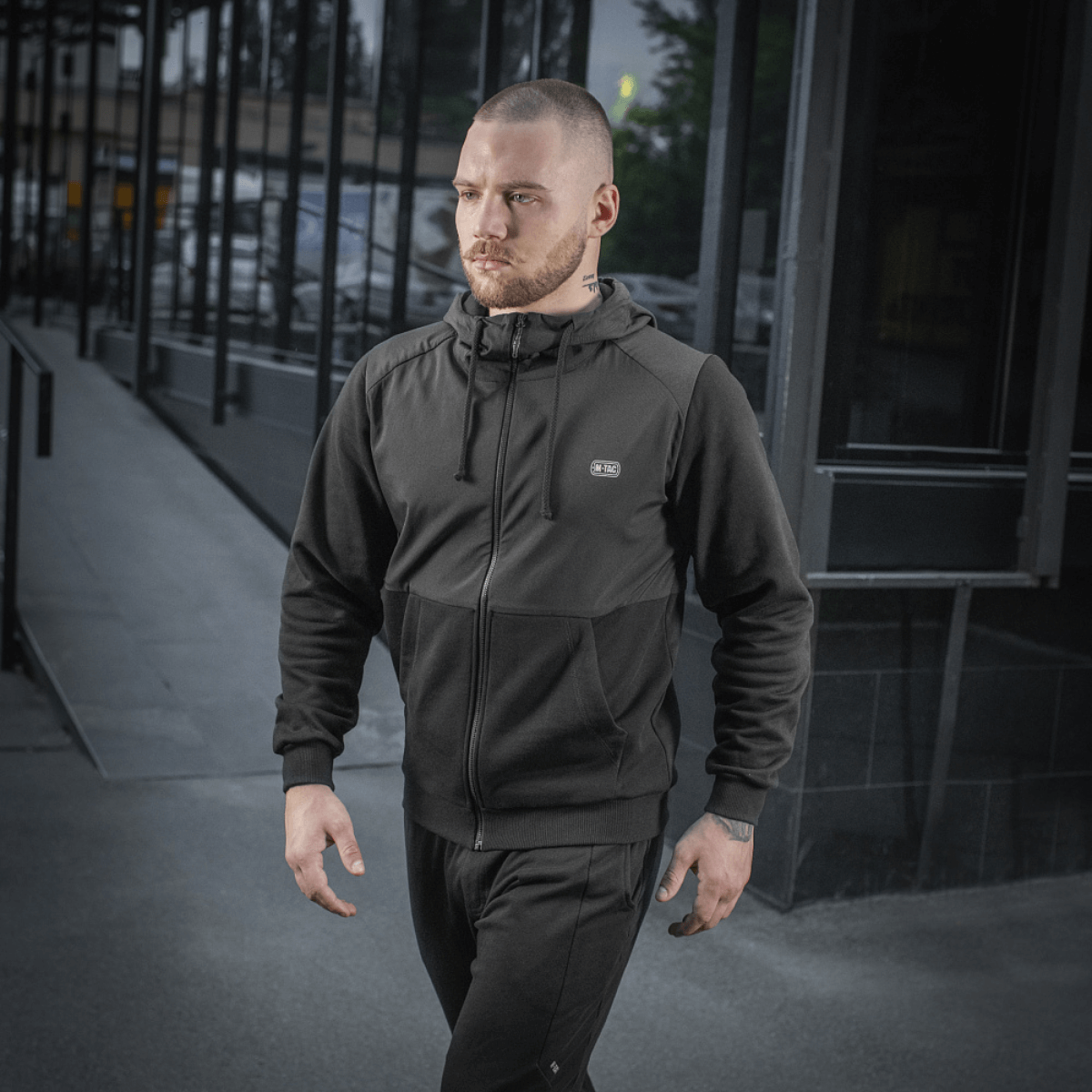 Mand iført M-Tac Pilgrim Bomberjakke, stilfuldt design med hætte, perfekt til hverdagsbrug og sport, den holdbare og komfortable jakke.