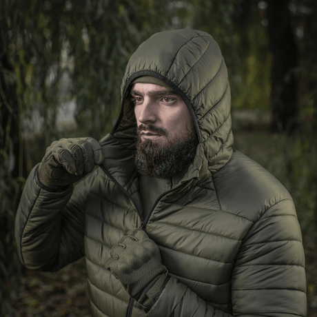 Mand iført M-Tac Stalker Gen.III Jakke i skovmiljø, viser jakke med hætte og lynlås, ideel til overgangssæsonen