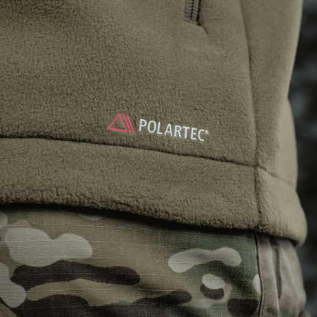 M-Tac Combat Fleece Polartec Jakke med Polartec logo og camouflagebukser, perfekt til taktisk brug, viser detaljer af materialet.
