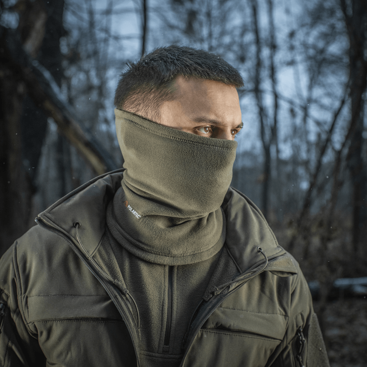 Mand bærer M-Tac Tube Scarf Polartec i skoven som ansigtsmaske, beskytter mod kulde og vind under udendørsaktiviteter.