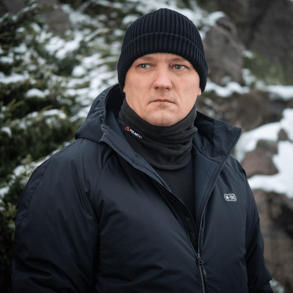 Mand iført M-Tac Tube Scarf Polartec som halstørklæde i vinterlandskab, varm og stilfuld til udendørs aktiviteter.