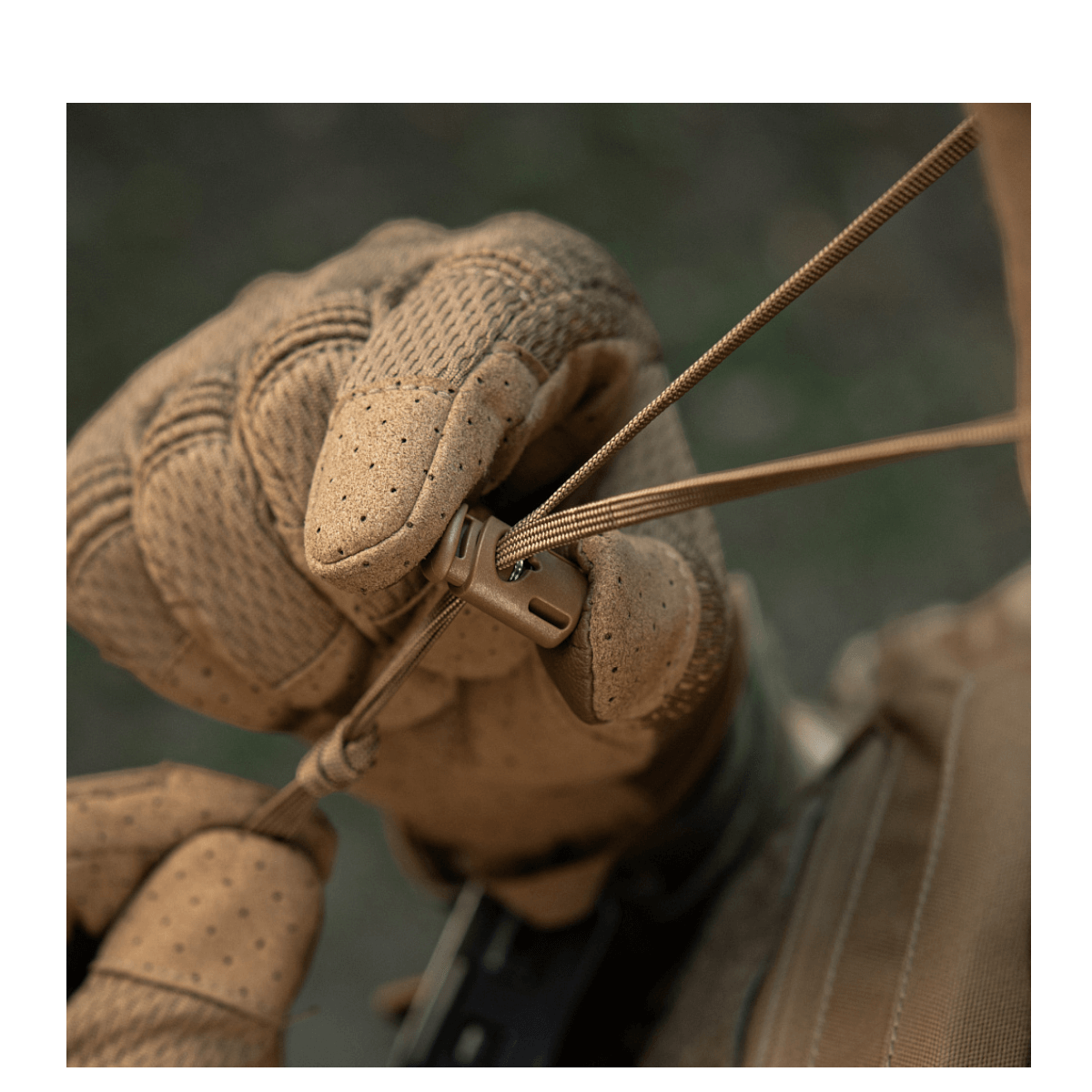Taktisk hånd med handsker justerer udstyrssnøre i feltmiljø.