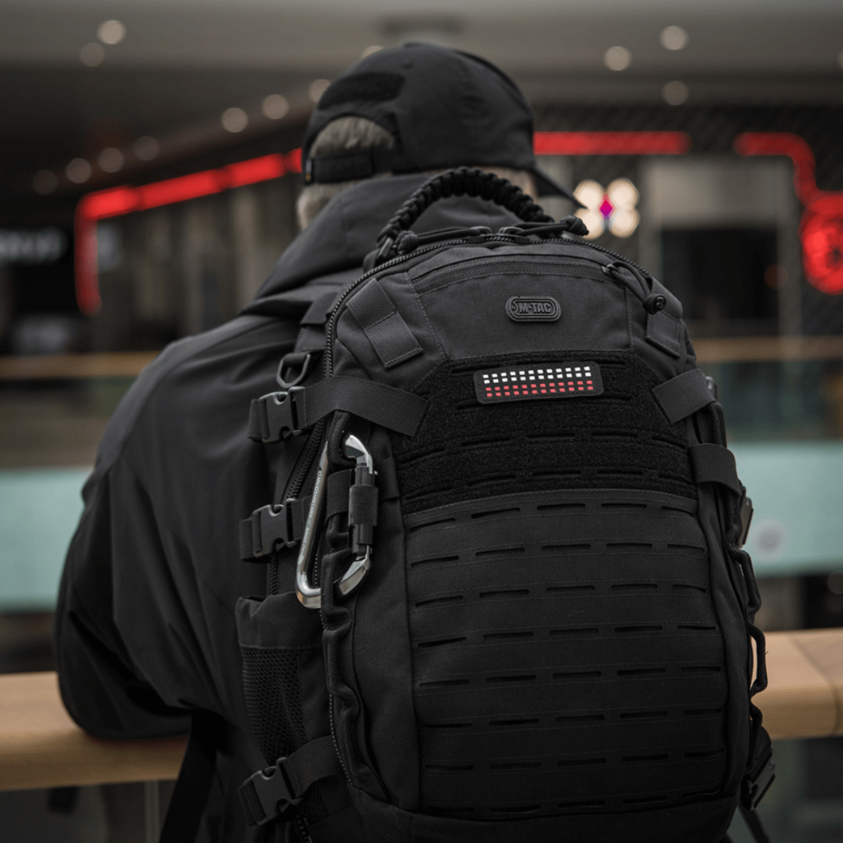 En person med rygsæk iført M-Tac Patch Flag 25x80 Mini Squares i slidstærk Cordura 500D med Velcro-beslag, passende til taktisk udstyr.