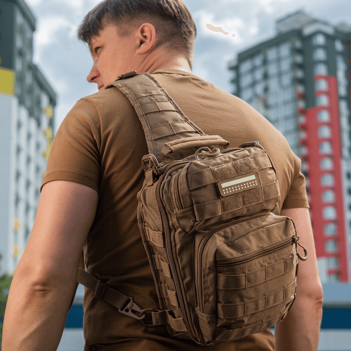 Mand med taktisk rygsæk udstyret med M-Tac Patch Flag 25x80 Mini Squares i bymiljø. Patchen sikrer stil og funktionalitet.