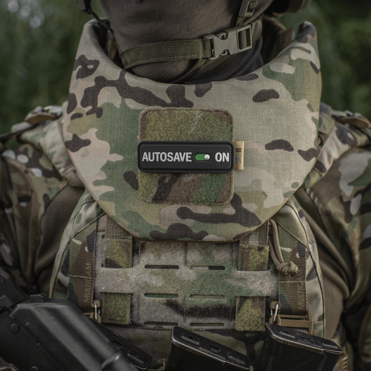 M-Tac Patch Autosave PVC i camouflage, monteret på militærvest for fokus og dedikation, med velcro bagside til nem fastgørelse.