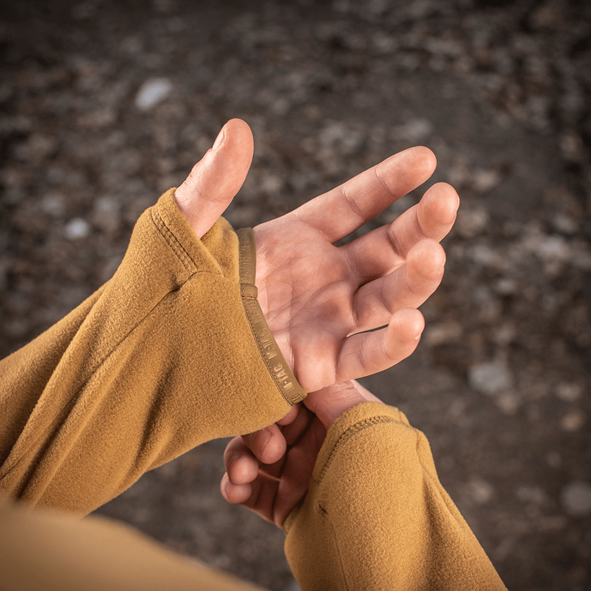 M-Tac Delta Polartec Fleecejakke viser tommelfingerhul i brug for ekstra komfort og varmeisolering. Beige fleecejakke detalje med en persons hænder.
