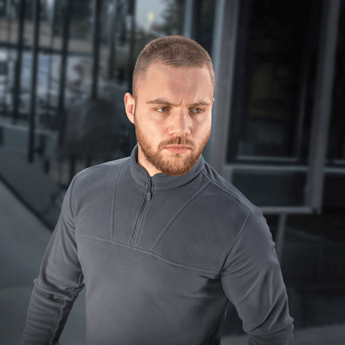 Mand iført M-Tac Delta Polartec Fleecejakke, en stilren og funktionel jakke i grå med halv lynlås, ideel til kolde dage.