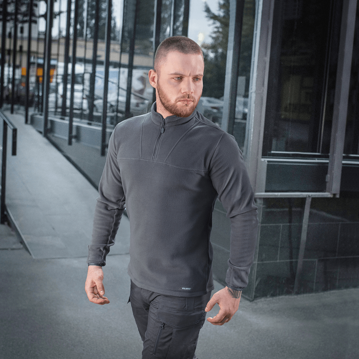 Mand iført M-Tac Delta Polartec Fleecejakke i grå med moderne baggrund, ideel til kolde dage med fremragende isoleringsmuligheder.