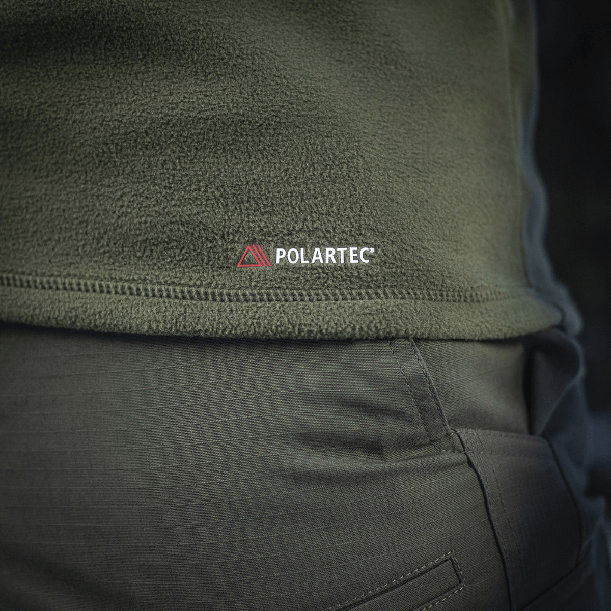 Nærbillede af M-Tac Delta Polartec Fleecejakke i olivengrøn med Polartec-logo, fremstillet af slidstærkt og åndbart Polartec® Micro Series-fleece.