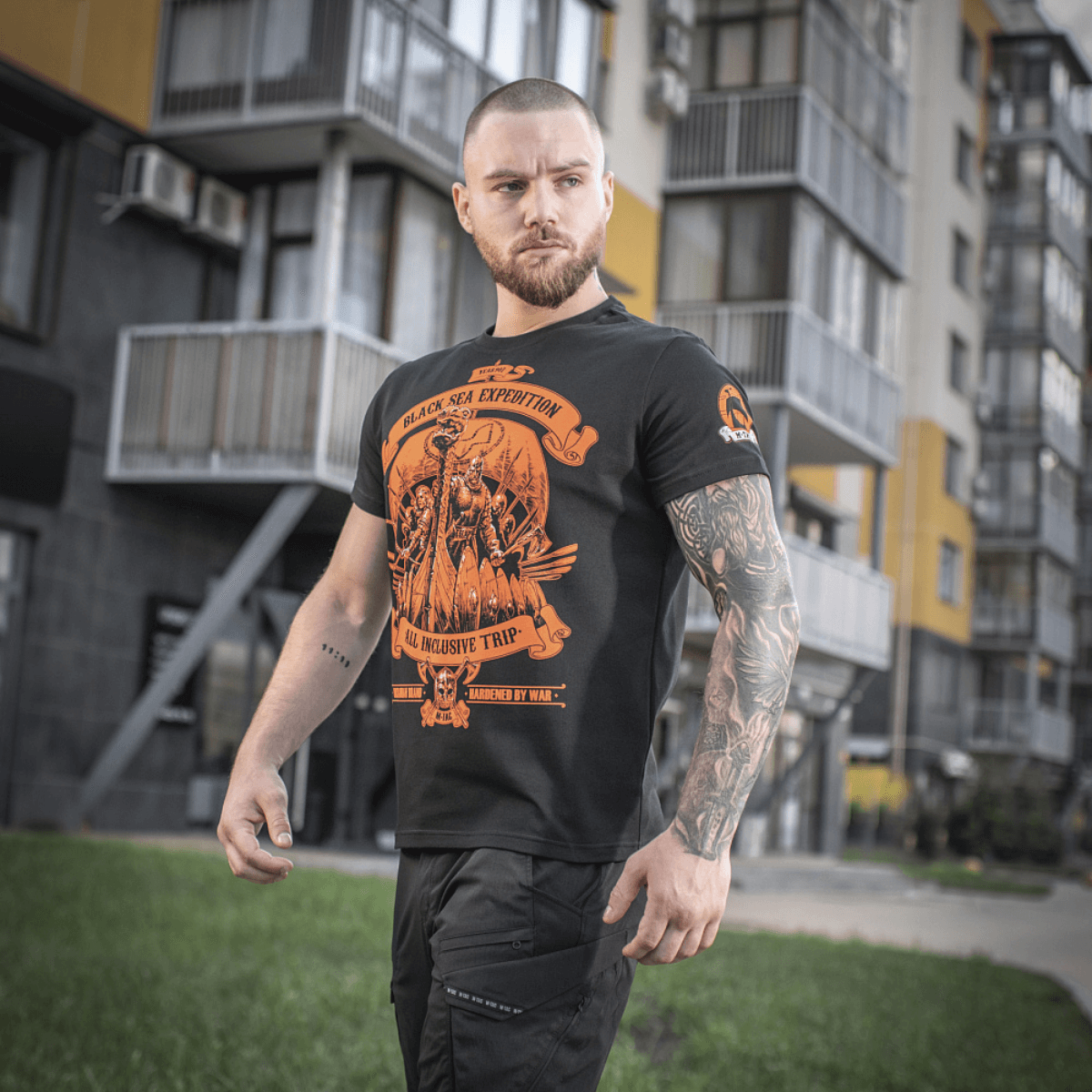 Mand iført M-Tac T-shirt Black Sea Expedition med unikt design foran bygninger, velegnet til aktiv livsstil og dagligt brug.