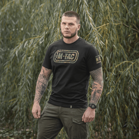 Mand iført M-Tac T-Shirt Logo med camouflage og slogans i naturen