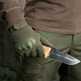 M-Tac Handsker Assault Tactical Mk.3 bæres af person der holder kniv, forstærket håndflade og dæmpende knoer synlige, tæt på.