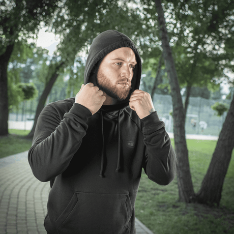 Mand iført M-Tac Hættetrøje Cotton Raglan i park, fremstillet i blødt bomuld med raglanærmer for optimal komfort og bevægelsesfrihed.