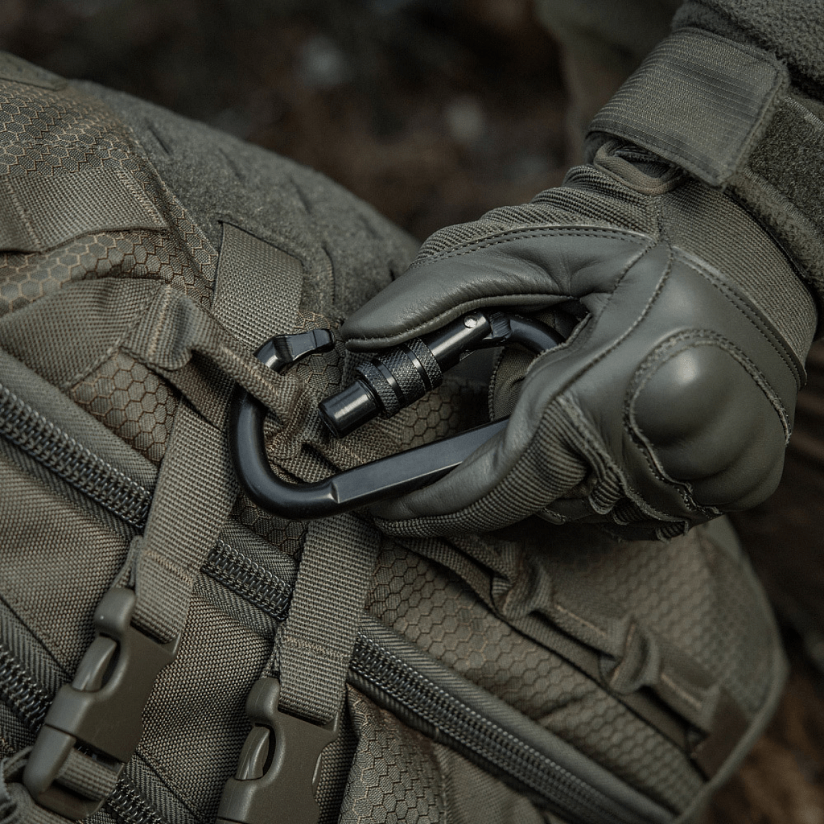 M-Tac Karabinhage 10 cm fastgjort til et taktisk taske, lavet af 40Cr legeret stål, ideel til reb og slynger, trapezformet design.