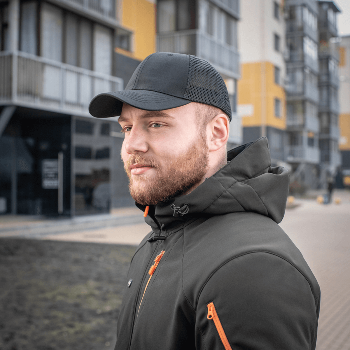 Mand iført M-Tac Mesh Flex Ripstop Baseball Cap foran moderne bygninger, perfekt til udendørs aktiviteter, sort kasket med mesh-paneler.
