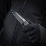 M-Tac Outdoor & Militær foldekniv - Type 6 holdt i en hånd iført sort handske, krom rustfrit stål klinge, G10-komposit håndtag.