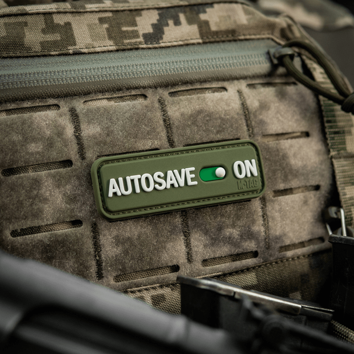 M-Tac Patch Autosave PVC 3D morale patch på en camouflage rygsæk, lavet af PVC, 8 x 2.5 cm, med fuld farve og velcro bagside.