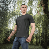 Mand iført M-Tac Raglan T-Shirt 93/7 foran grøn baggrund, materiale 93% bomuld 7% elastan, stilfuld og åndbar t-shirt i sort.