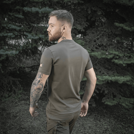 Mand i M-Tac Sniper T-shirt i naturmiljø, viser rygsiden og fremhæver elasticitet og pasform.