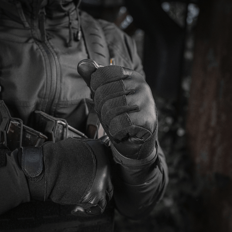 En person iført M-Tac Handsker Police Gen.2 med taktisk udstyr og hættejakke i en mørk udendørs setting.