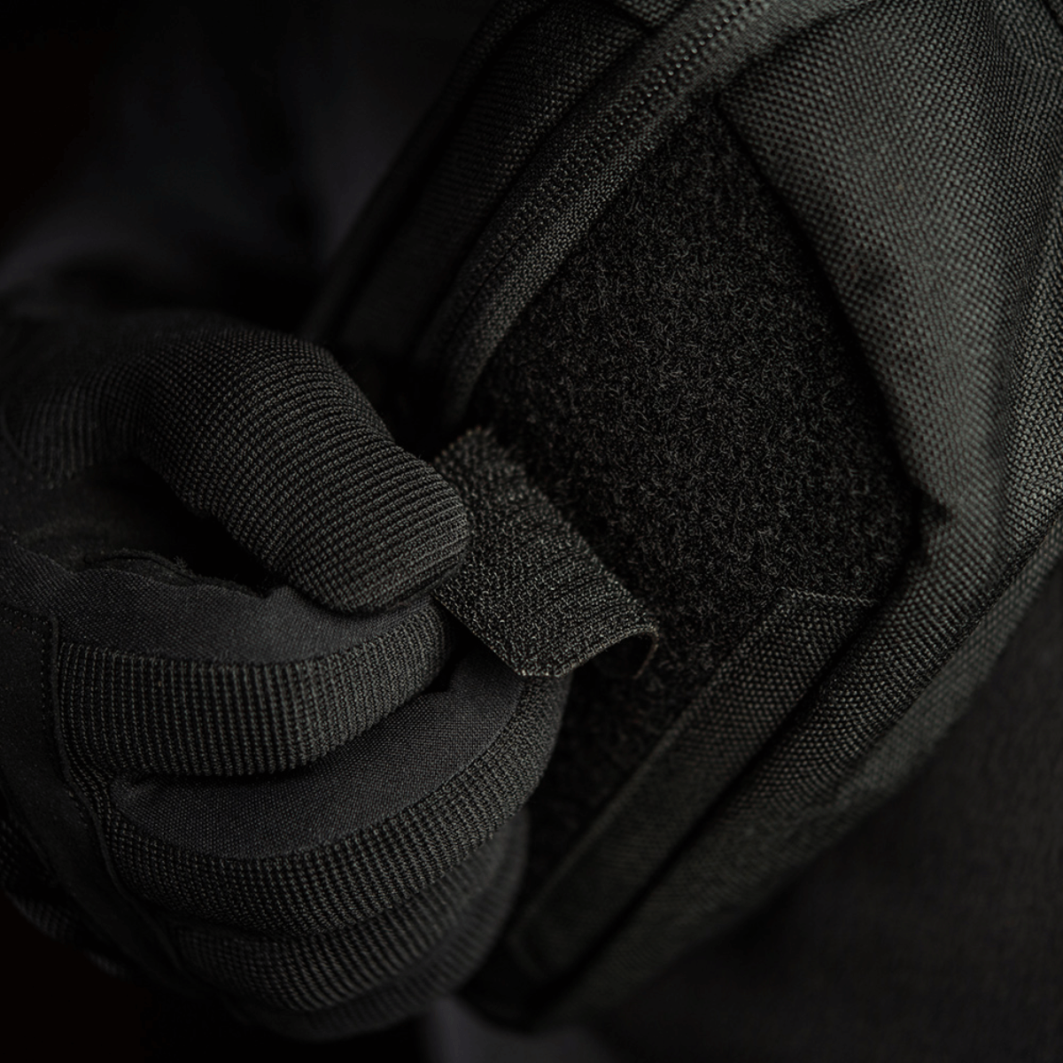 Person iført sort handske justerer M-Tac Patch Valknut Laser Cut Odin symbol på en jakke. Taktisk udstyr med velcro.