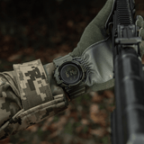 M-Tac Tactical Ur med Kompas 2233 båret af soldat i skov, viser funktionalitet for outdoor og taktisk brug, med holdbart design og kompas.