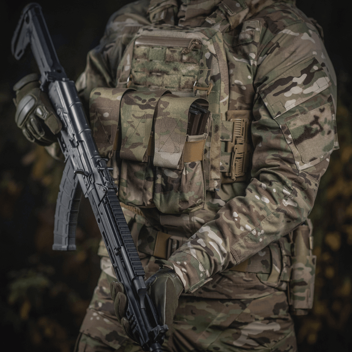 Person i camouflageuniform med M-Tac taske til 2 magasiner i brug og gevær i hænderne, illustrerer taktisk militærudstyr.