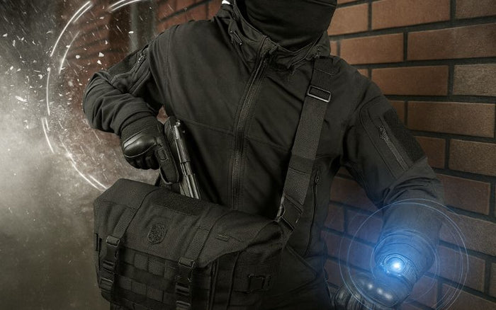 Mand i sort tøj og hætte holder en taske og står ved en murstensvæg, lysende cirkel i baggrunden