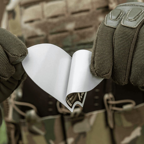 M-Tac Sticker Valkyrie holdt af person i camouflage, klar til brug. Viser den beslutsomme krigsgudinde med M4 gevær på Arrowhead patch.